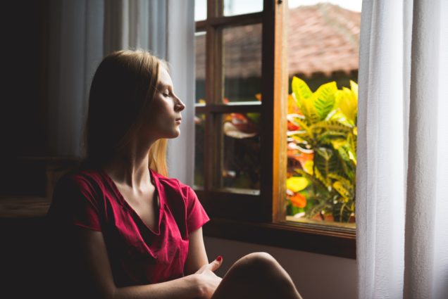 Take a breather. Woman sitting relaxing next to open window with plants in view.